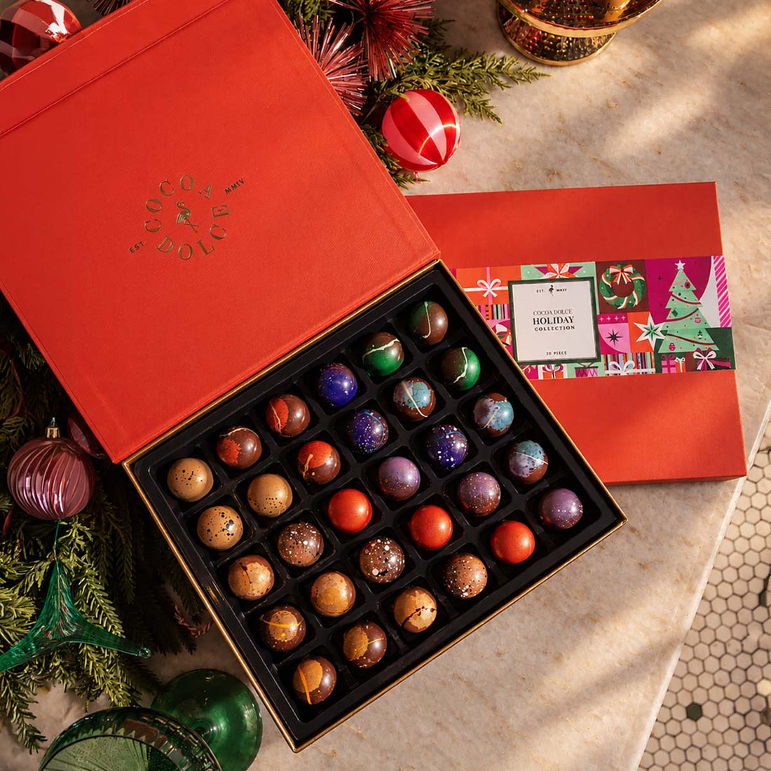 Cocoa Dolce 30-Piece Holiday Collection gift box with assorted handcrafted chocolates, festive red packaging, and holiday decorations.